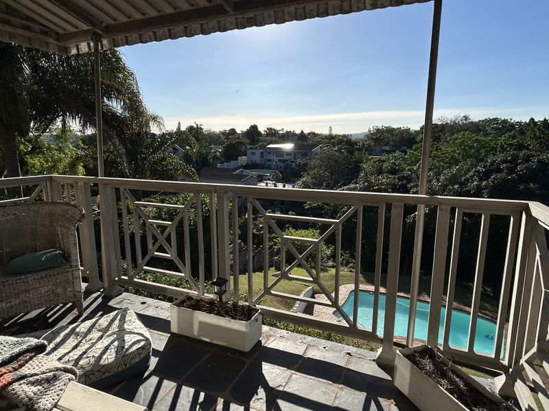 Covered balcony featuring slate flooring and a metal balustrade, offering elevated views over the garden and swimming pool.