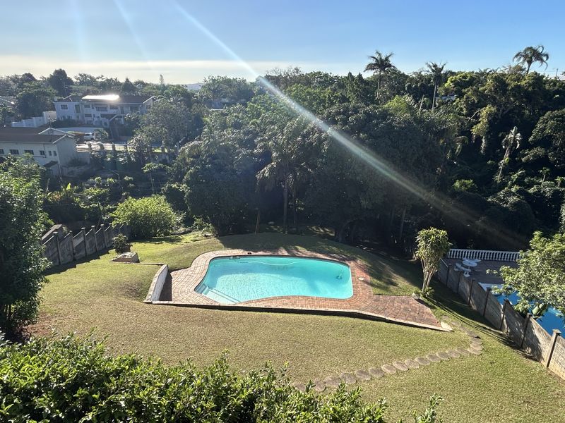 Elevated view of a swimming pool set within a landscaped garden, featuring a brick surround and surrounding greenery.