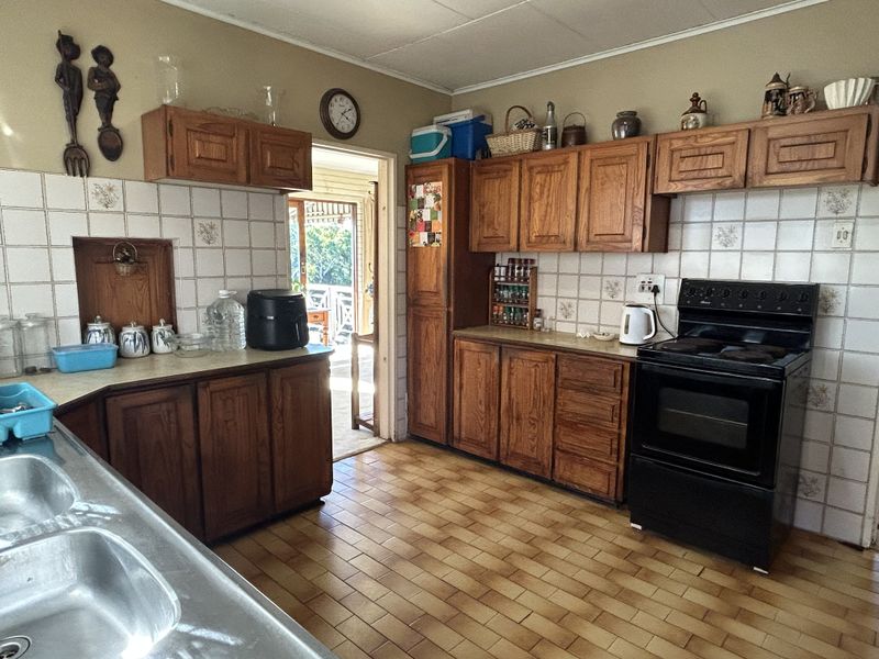 A dated kitchen featuring wooden cabinetry, tiled backsplash, and a freestanding electric stove, with direct access to an outdoor patio area.