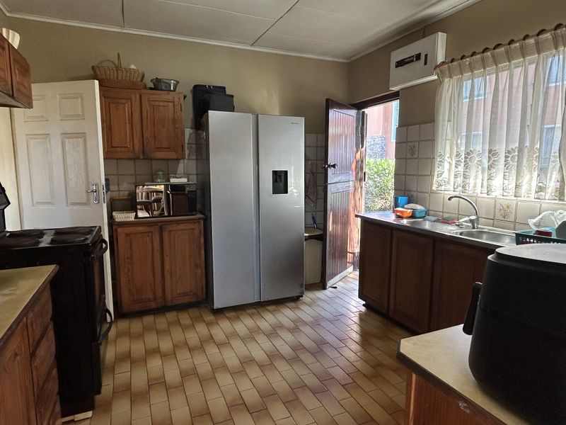 A functional kitchen featuring wooden cabinetry, tiled backsplash, and tiled flooring with direct access to the exterior.