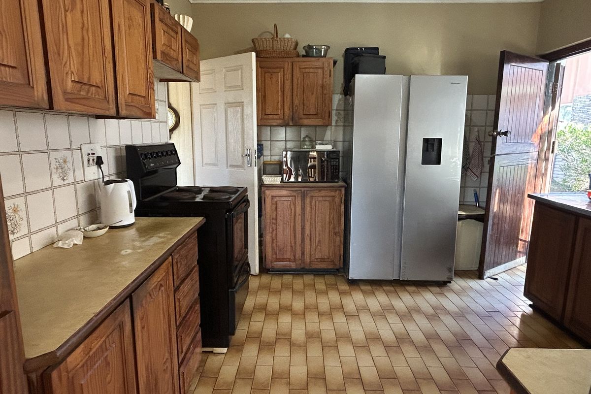 A functional kitchen featuring traditional wooden cabinetry, tiled backsplash, and tiled flooring, offering a classic layout with direct access to the exterior.