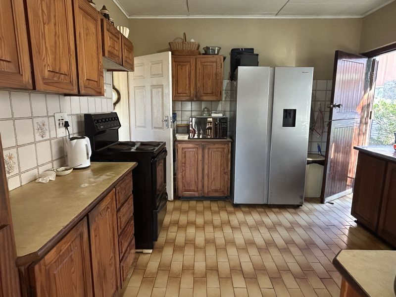 A functional kitchen featuring traditional wooden cabinetry, tiled backsplash, and tiled flooring, offering a classic layout with direct access to the exterior.