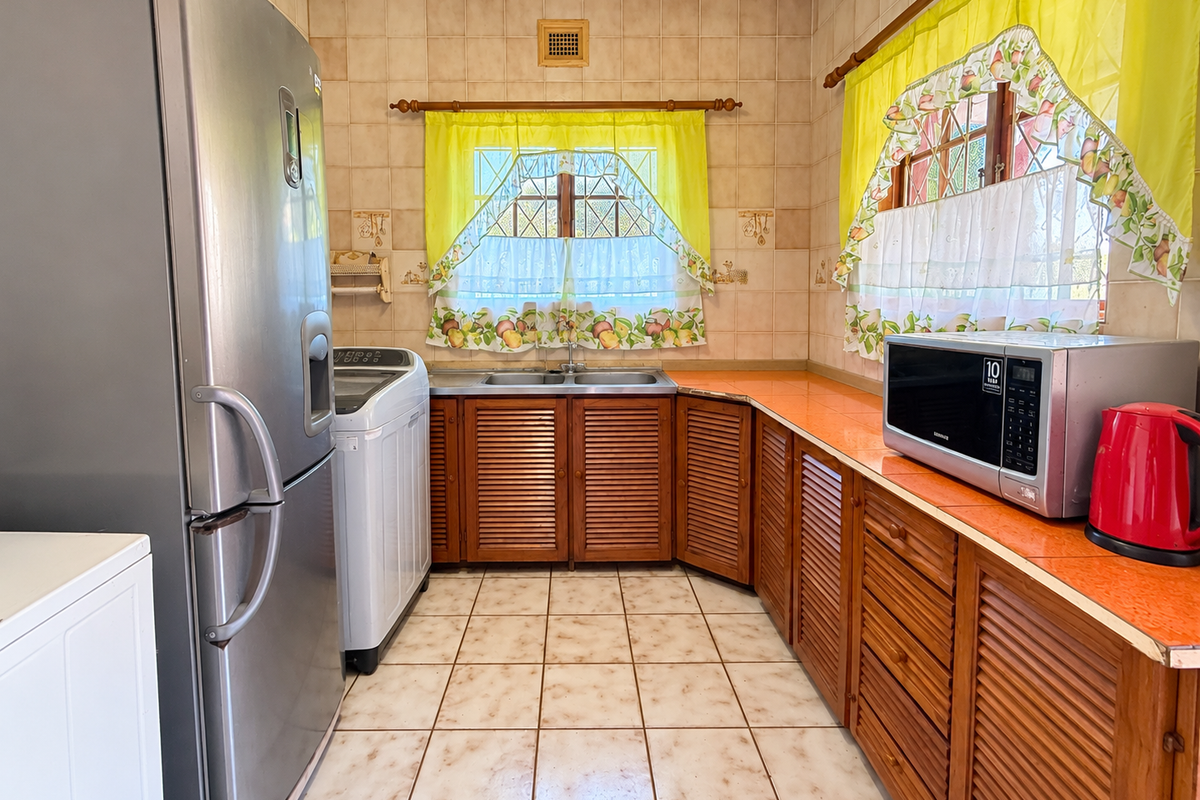 A functional kitchen featuring louvered wooden cabinetry, tiled countertops, and a double basin sink, offering a classic layout with ample storage space.