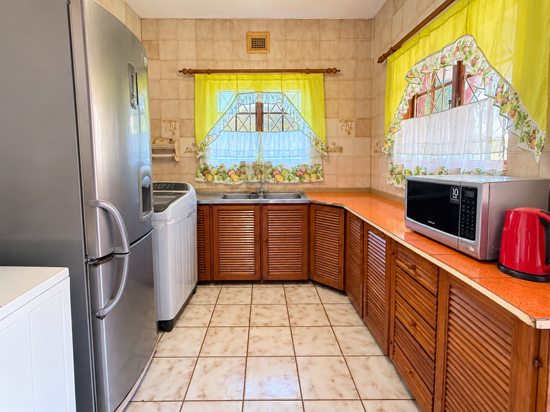 A functional kitchen featuring louvered wooden cabinetry, tiled countertops, and a double basin sink, offering a classic layout with ample storage space.