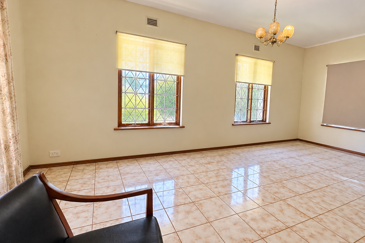 A spacious, light-filled living room featuring neutral walls, ceramic tile flooring, and classic leaded glass windows with roller blinds.