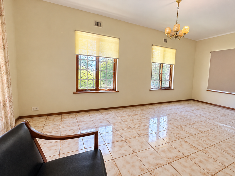 A spacious, light-filled living room featuring neutral walls, ceramic tile flooring, and classic leaded glass windows with roller blinds.