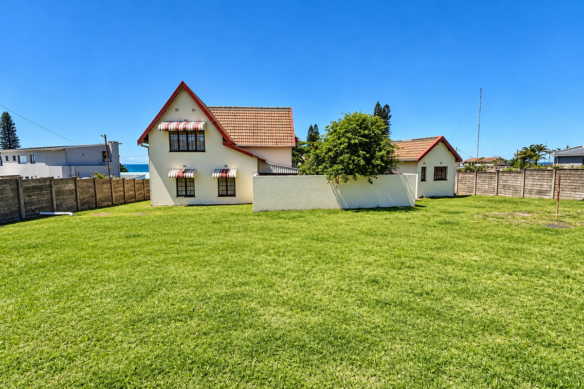 A spacious rear garden view featuring a detached house with a tiled roof, concrete boundary walls, and classic window awnings.