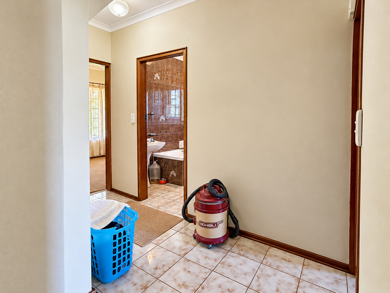 A clean, tiled hallway providing access to a bathroom and adjacent rooms, featuring neutral wall tones and timber door frames.