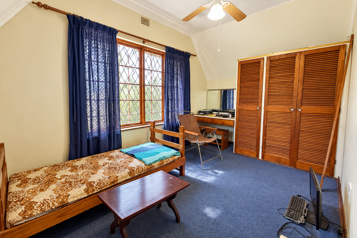A bedroom featuring a built-in wooden wardrobe, vanity, ceiling fan, and leaded glass windows, offering a functional space with potential for modernization.