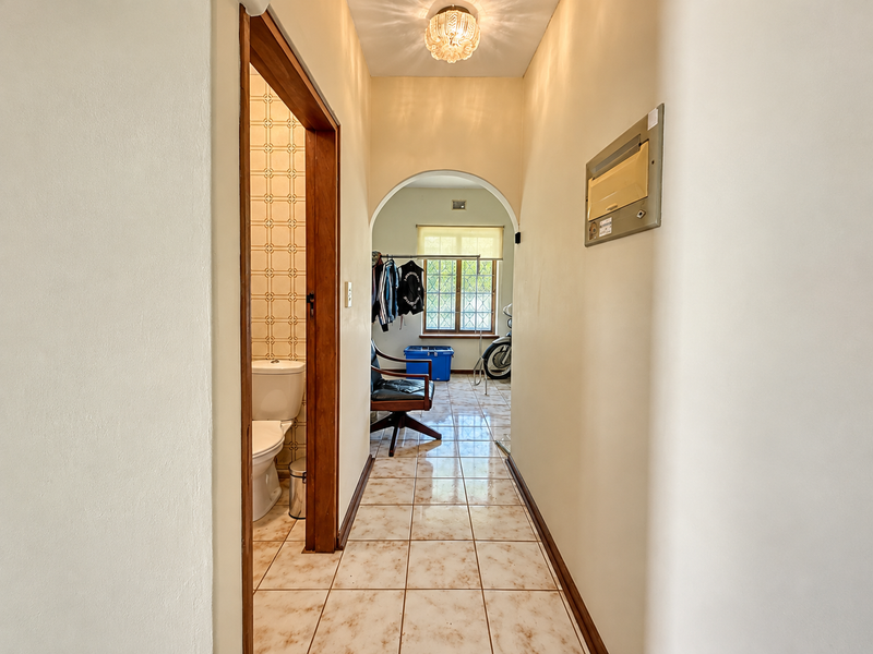 A tiled hallway featuring an arched transition, a wall-mounted electrical distribution board, and access to an adjacent bathroom.