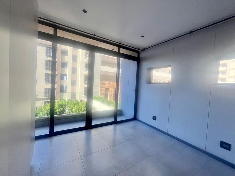 A bright, modern, and empty bedroom featuring large sliding glass doors that open to a balcony, tiled floors, and recessed lighting.