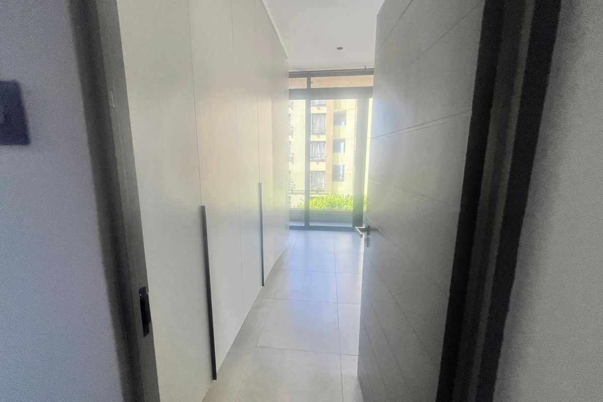 A bright, modern hallway featuring extensive built-in cupboard storage, sleek tiled flooring, and a sliding glass door leading to an outdoor area.