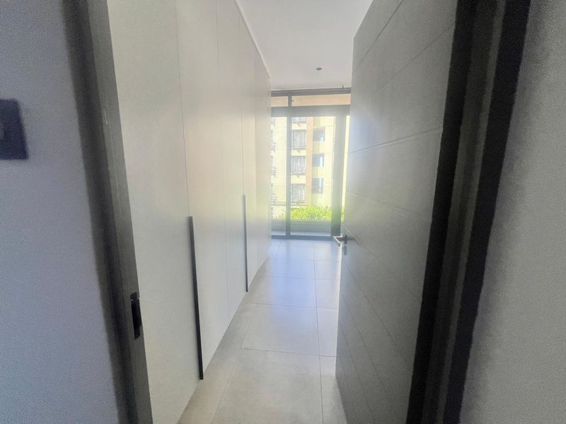 A bright, modern hallway featuring extensive built-in cupboard storage, sleek tiled flooring, and a sliding glass door leading to an outdoor area.