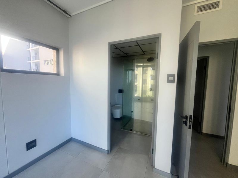 A clean, empty bedroom featuring neutral tiled flooring, modern grey door frames, and an en-suite bathroom entrance with glass shower enclosure.