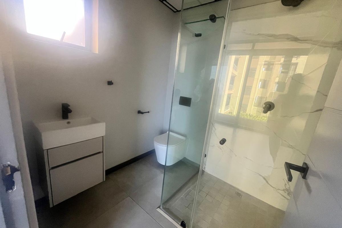 Modern bathroom featuring a wall-mounted vanity, wall-hung toilet, and a spacious glass-enclosed shower with contemporary black fixtures and marble-look tiling.