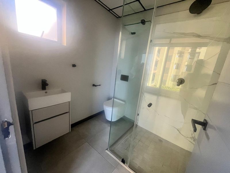 Modern bathroom featuring a wall-mounted vanity, wall-hung toilet, and a spacious glass-enclosed shower with contemporary black fixtures and marble-look tiling.