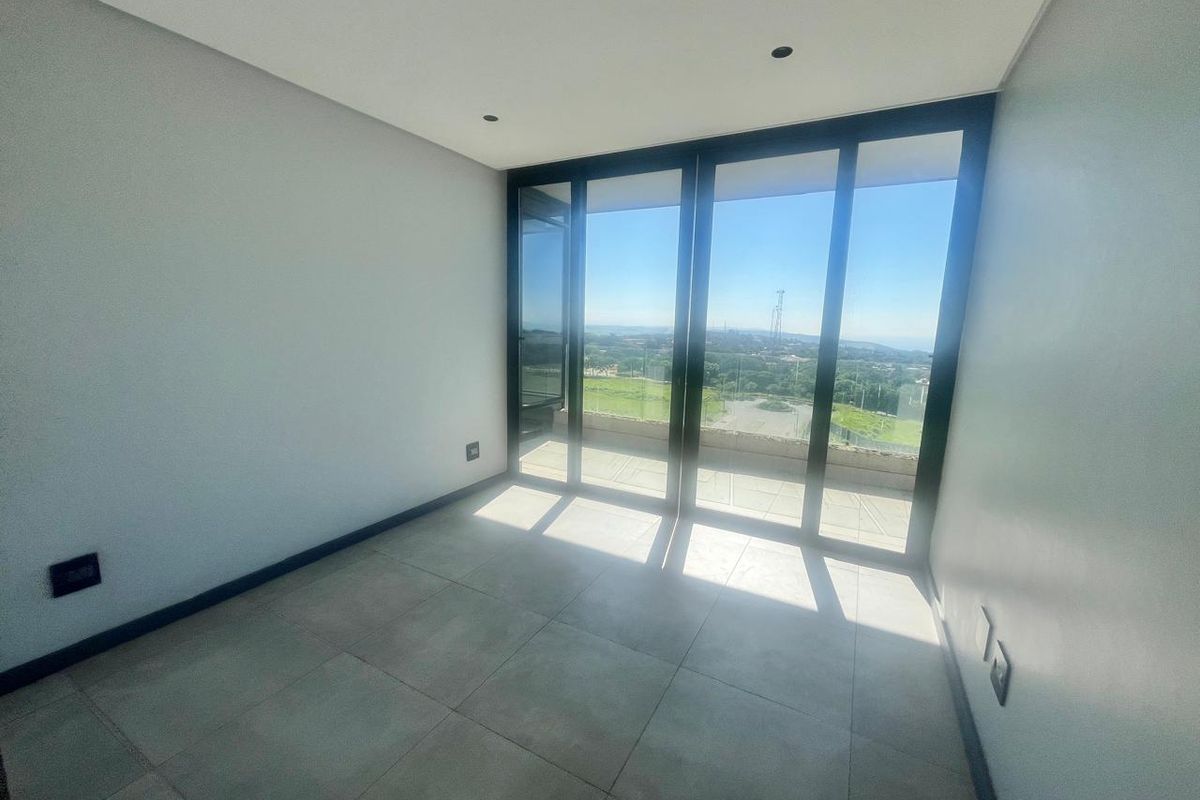 A bright, empty bedroom featuring large sliding glass doors that open onto a balcony with expansive views and modern tiled flooring.