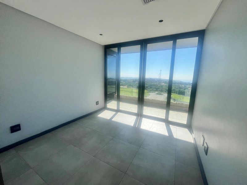 A bright, empty bedroom featuring large sliding glass doors that open onto a balcony with expansive views and modern tiled flooring.