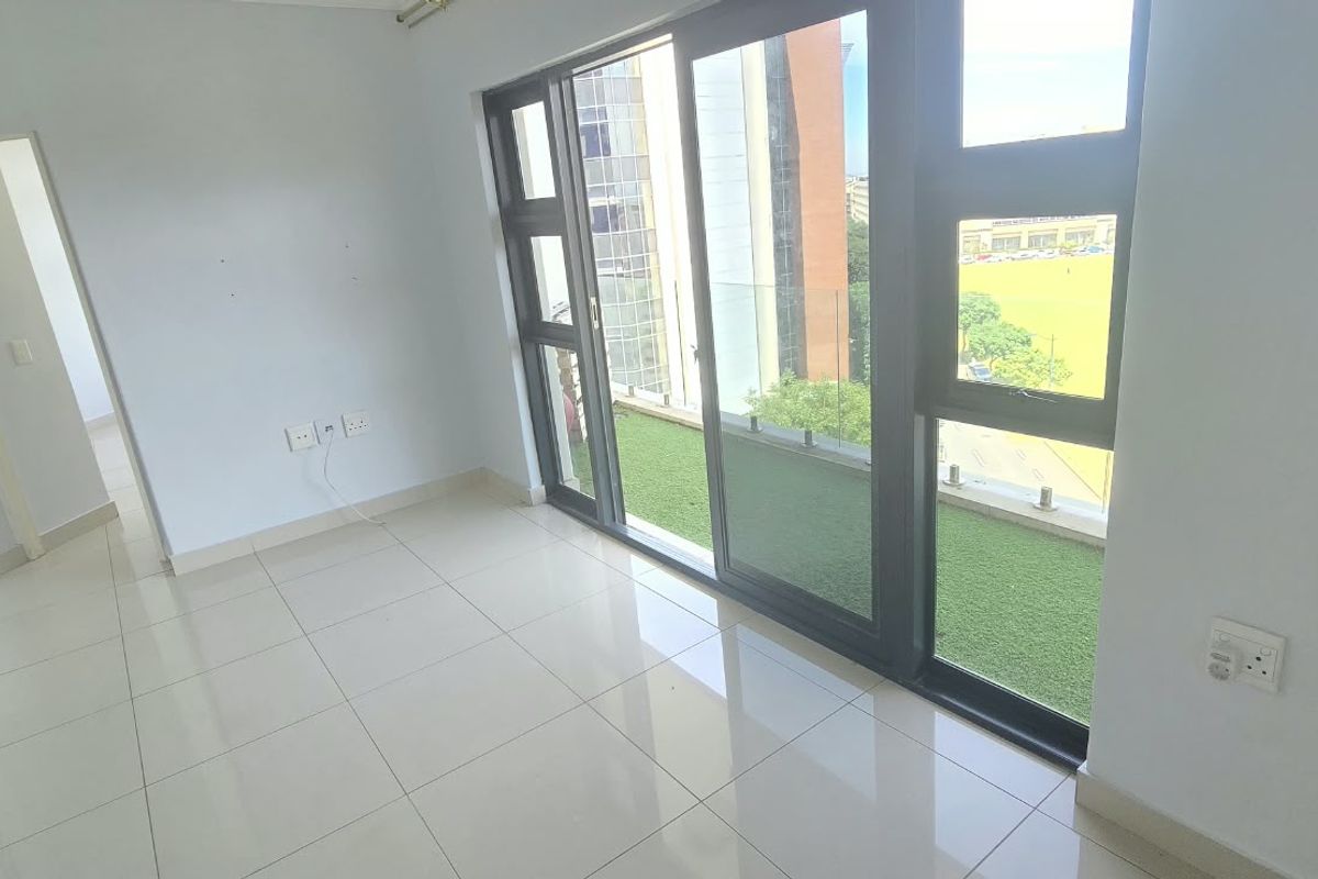 A bright, empty living area featuring large sliding glass doors that open onto a balcony, with neutral tiled flooring and modern finishes.