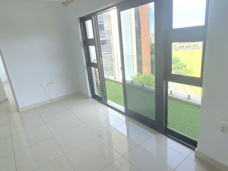 A bright, empty living area featuring large sliding glass doors that open onto a balcony, with neutral tiled flooring and modern finishes.