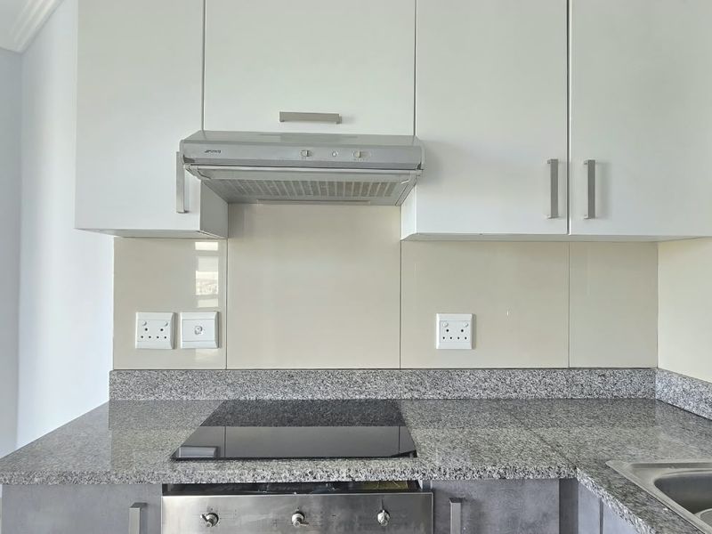A clean, modern kitchen featuring granite countertops, a built-in oven with electric hob, stainless steel extractor fan, and ample upper cabinetry.