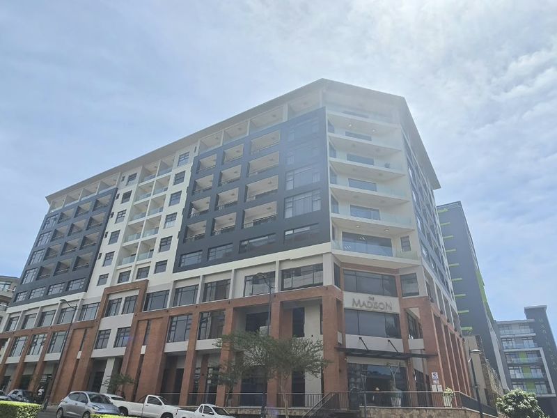 A modern multi-story apartment building featuring a brick facade, glass balconies, and large windows, situated in a contemporary urban development.