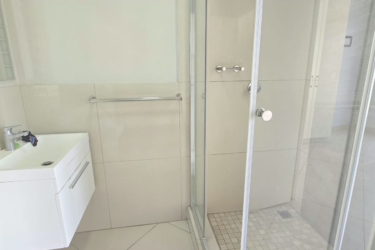 A clean, modern bathroom featuring a wall-mounted vanity, basin, and a glass-enclosed shower with neutral wall and floor tiling.