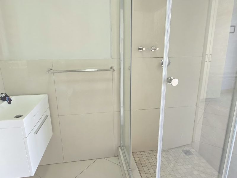 A clean, modern bathroom featuring a wall-mounted vanity, basin, and a glass-enclosed shower with neutral wall and floor tiling.