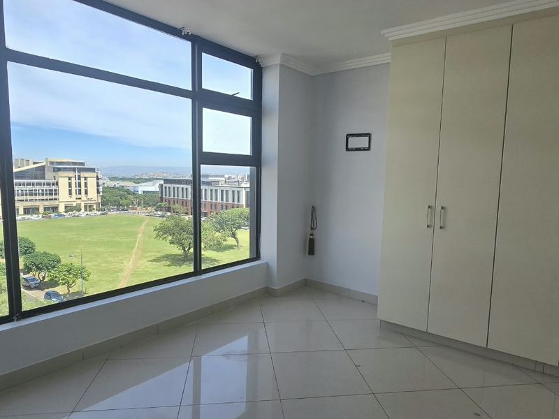 A bright, empty bedroom featuring large floor-to-ceiling windows with expansive views, tiled flooring, and ample built-in cupboard storage.