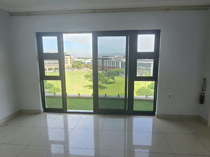 An empty living room featuring tiled flooring and a large sliding glass door that provides access to a balcony with scenic views.