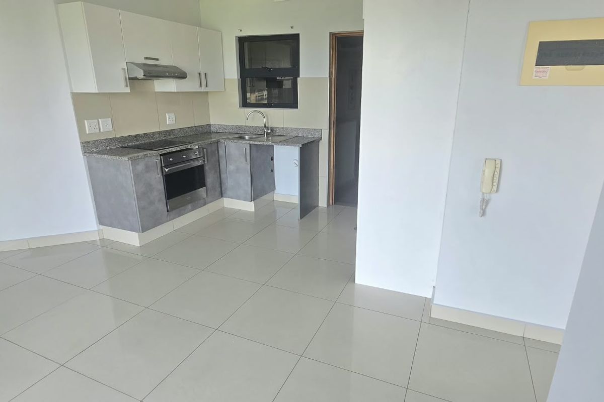 A clean, modern kitchen featuring granite countertops, built-in oven and hob, and neutral tiled flooring in an open-plan layout.