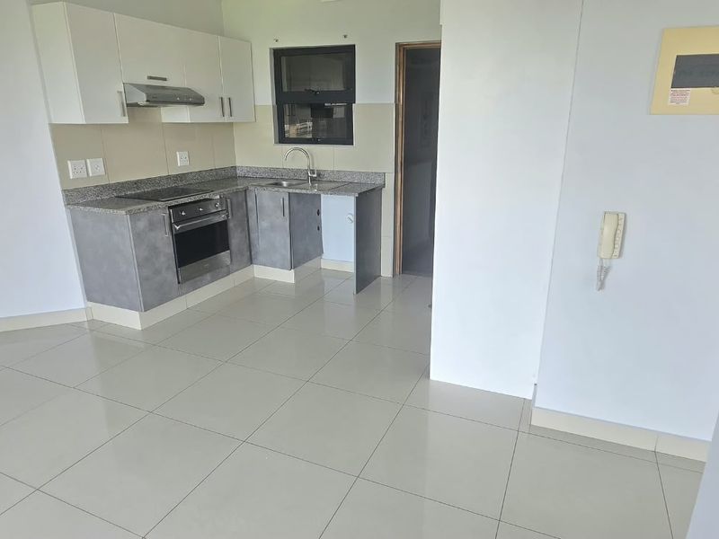 A clean, modern kitchen featuring granite countertops, built-in oven and hob, and neutral tiled flooring in an open-plan layout.