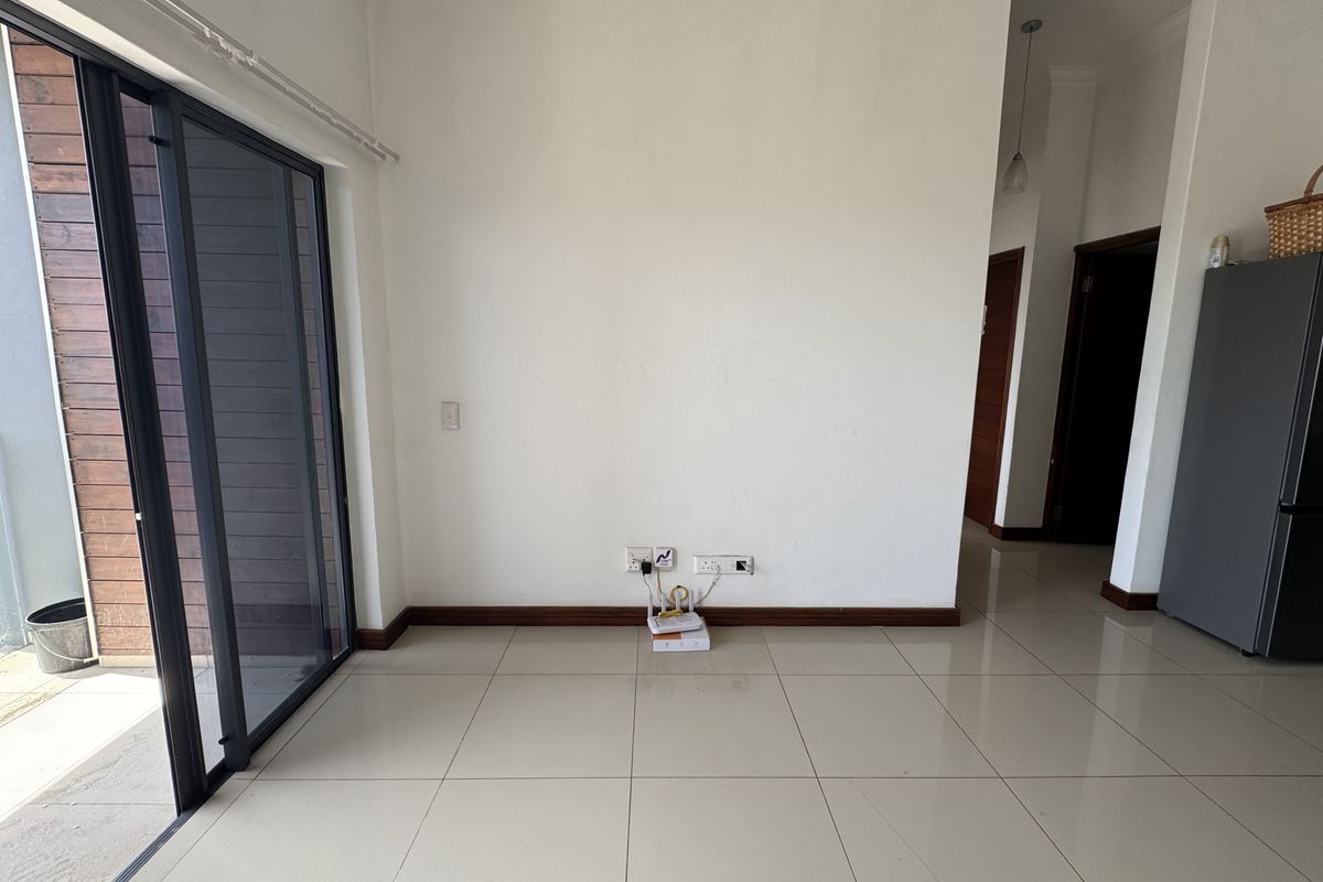 A bright, empty living area featuring large sliding glass doors, neutral tiled flooring, and clean white walls, providing a versatile space for customization.