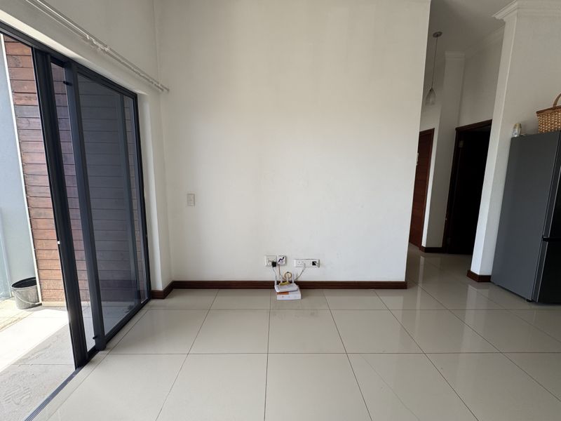 A bright, empty living area featuring large sliding glass doors, neutral tiled flooring, and clean white walls, providing a versatile space for customization.