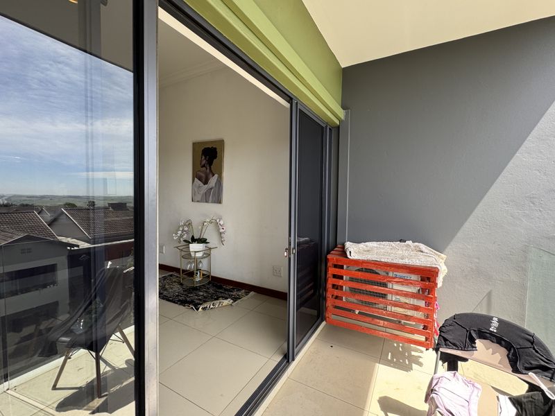 A modern balcony featuring tiled flooring, a glass balustrade, and sliding glass doors providing seamless access to the interior living space.