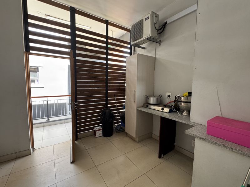 A compact kitchen area featuring granite countertops, built-in cabinetry, and an air conditioning unit, with direct access to an outdoor balcony through a timber screen.