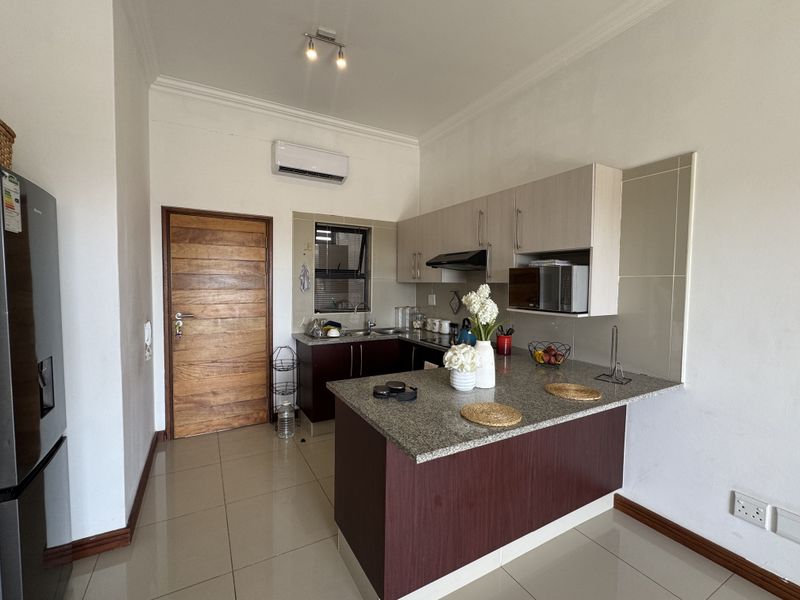 A well-maintained kitchen featuring granite countertops, built-in cabinetry, a tiled backsplash, and an integrated microwave, complemented by neutral tiled flooring.