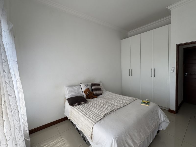 A well-maintained bedroom featuring neutral tiled flooring, crisp white walls, and ample built-in cupboard storage.