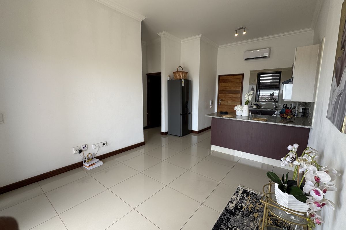 An open-plan living and kitchen area featuring tiled flooring, a breakfast bar with granite countertops, and a wall-mounted air conditioning unit.