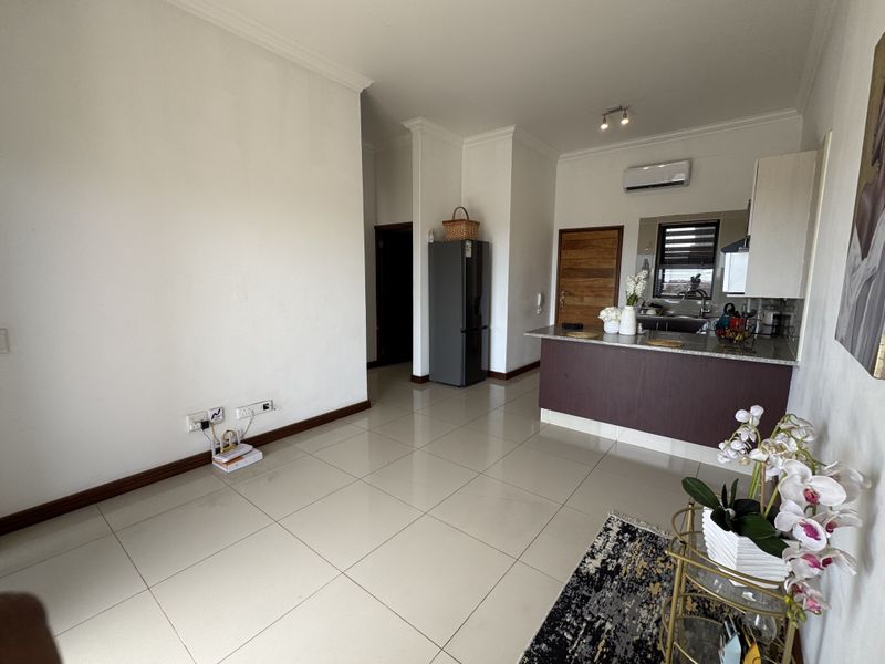 An open-plan living and kitchen area featuring tiled flooring, a breakfast bar with granite countertops, and a wall-mounted air conditioning unit.