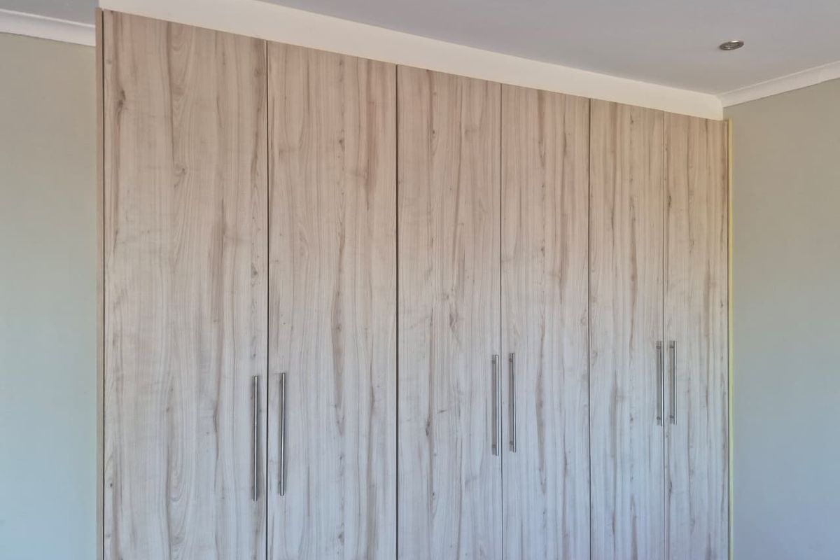 A bedroom featuring modern, light wood-grain built-in cupboards with sleek metal handles and recessed ceiling lighting.