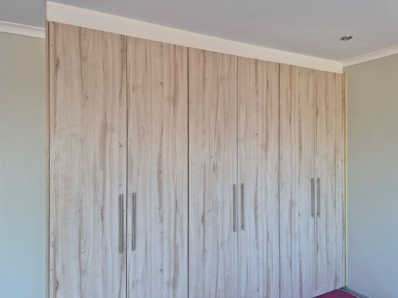 A bedroom featuring modern, light wood-grain built-in cupboards with sleek metal handles and recessed ceiling lighting.