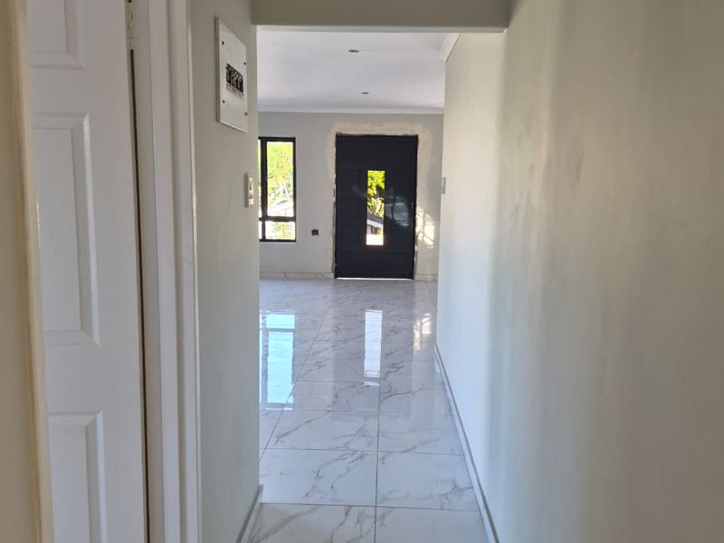 A bright, empty hallway featuring modern marble-look porcelain floor tiles, recessed lighting, and neutral wall finishes leading into an open-plan living area.