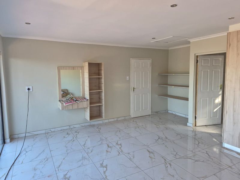 A bright, empty bedroom featuring modern marble-look tiled flooring, built-in vanity, shelving, and recessed lighting, offering a clean and neutral canvas.