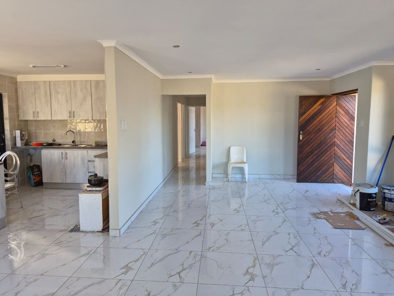 Open-plan living area featuring polished marble-look floor tiles, a modern kitchen with built-in cabinetry, and a distinctive chevron-pattern wooden front door.