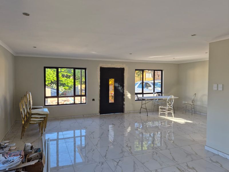 Spacious living area featuring polished porcelain floor tiles, recessed lighting, and large aluminium windows, currently awaiting final finishing touches around the entrance door.