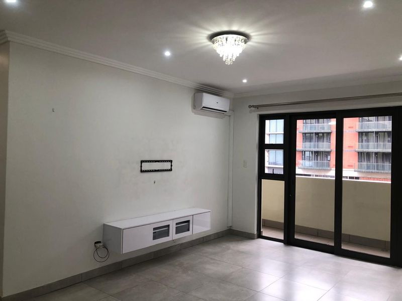 A bright, modern living room featuring tiled floors, a wall-mounted media console, air conditioning, and sliding glass doors leading to a balcony.