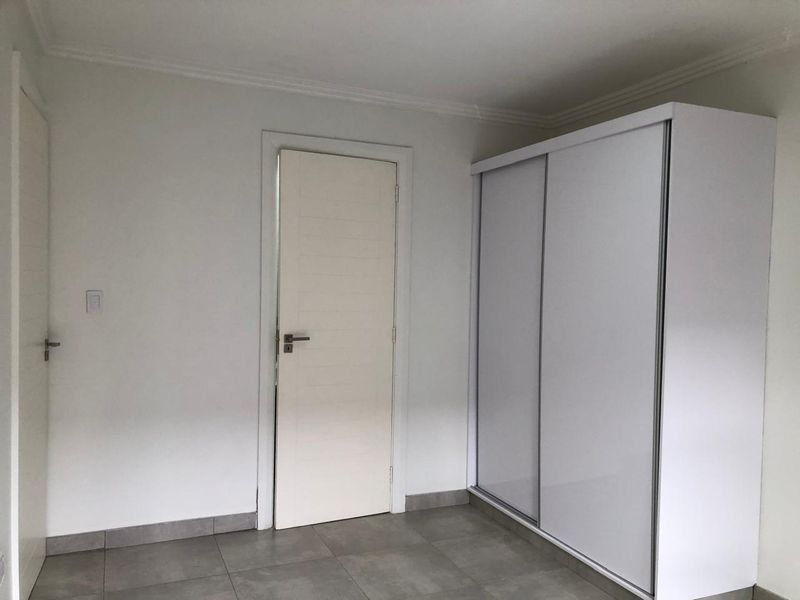 A clean, minimalist bedroom featuring neutral tiled flooring, white walls, and a modern built-in sliding door wardrobe.