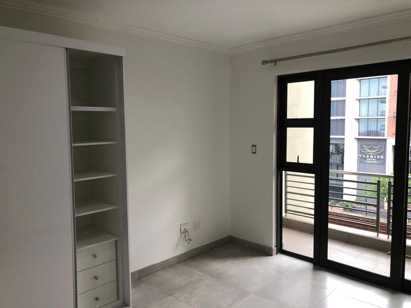A bright, empty bedroom featuring tiled floors, a built-in cupboard, and a sliding glass door providing access to a balcony.