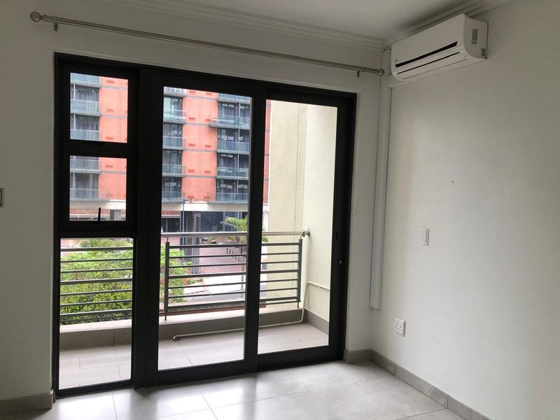 A bright, empty living area featuring tiled floors, a wall-mounted air conditioning unit, and large sliding glass doors leading to a private balcony.